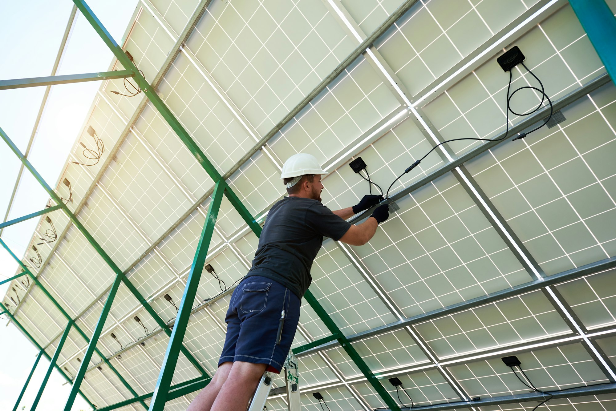 Professional worker installing solar panels on the green metal construction